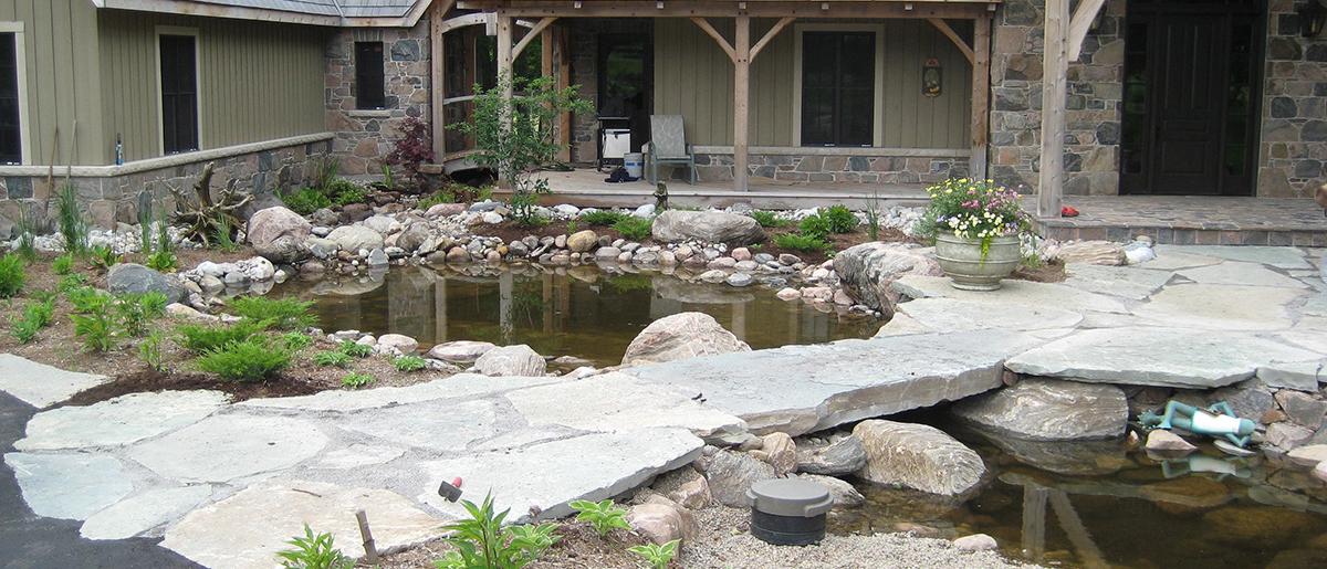 Custom pond water feature in a backyard by Johnston's Greenhouse